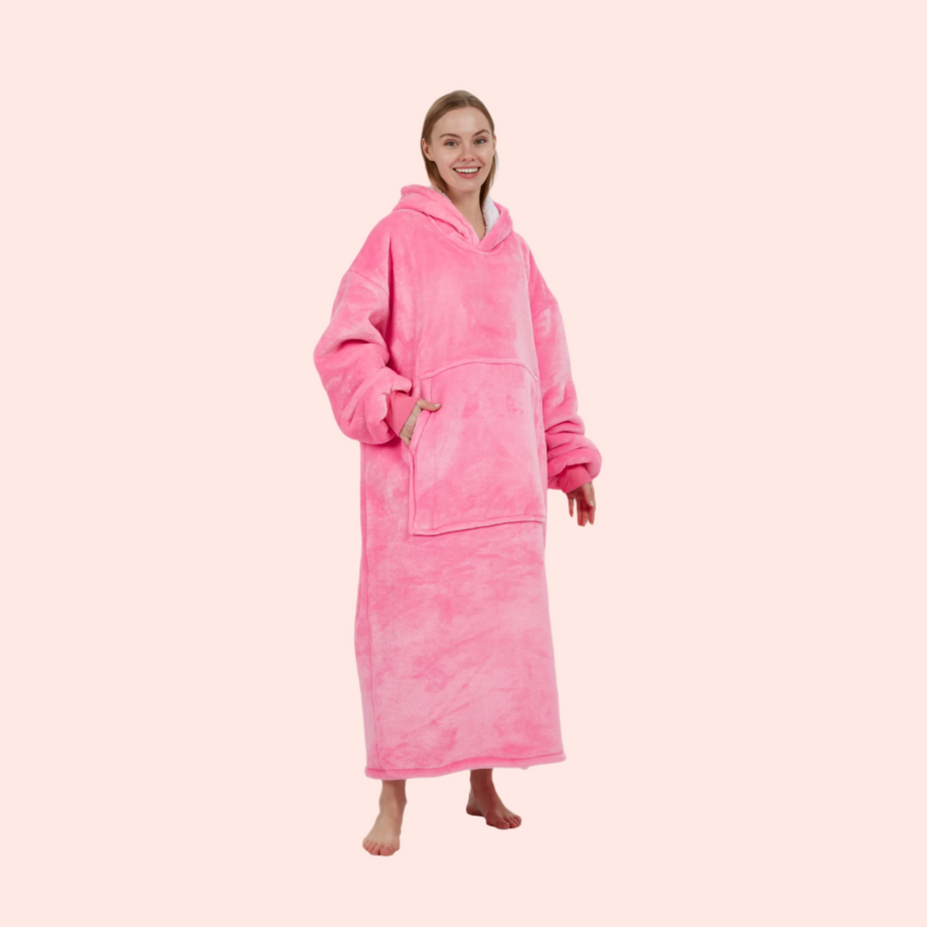 Model smiling in bright pink wearable blanket, slightly turned with hand in pocket.
