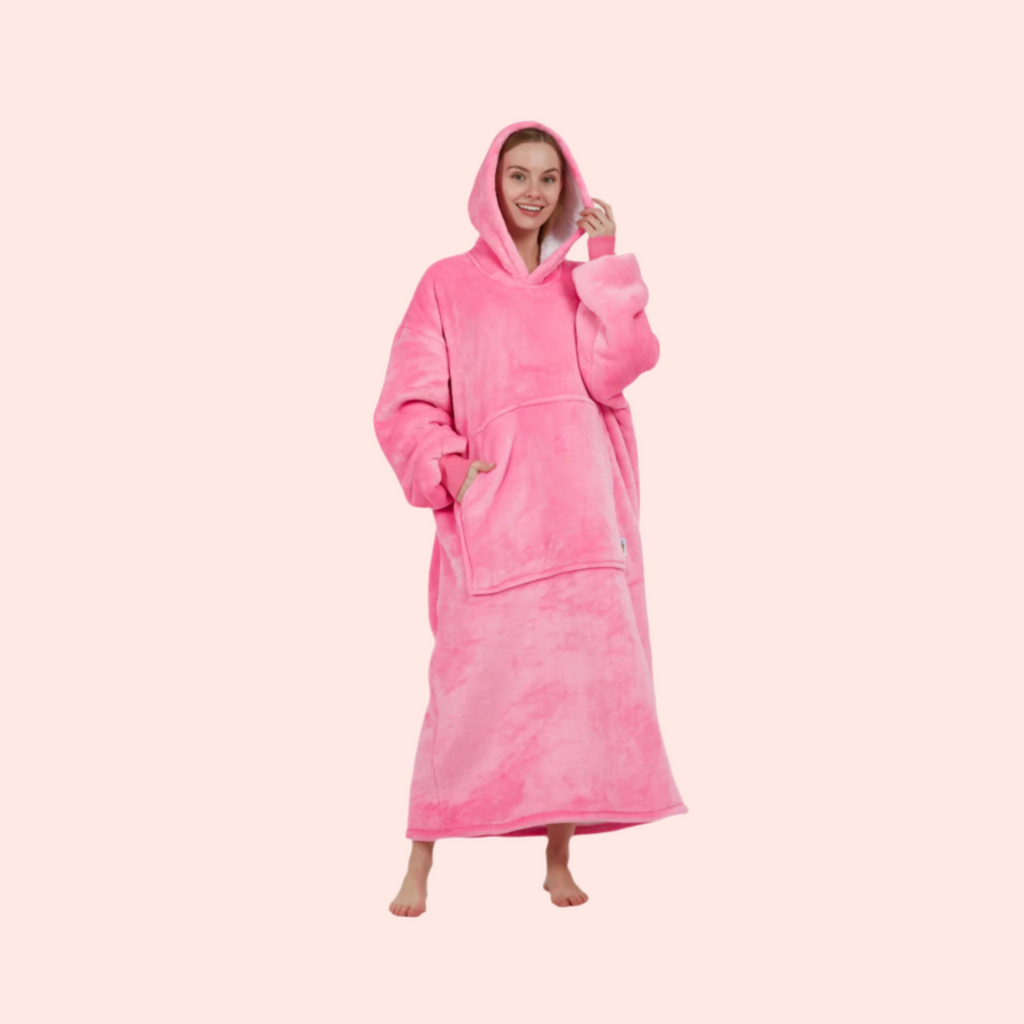 miling woman in full-length bright pink hoodie blanket standing on pale peach background.