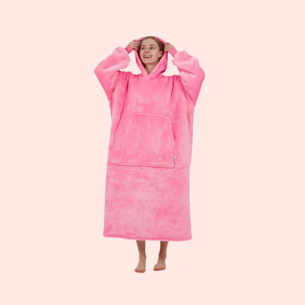Woman lifting hood of oversized pink wearable blanket with relaxed pose.